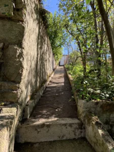 Allée bétonnée en pente, entre mur de soutènement et jardin