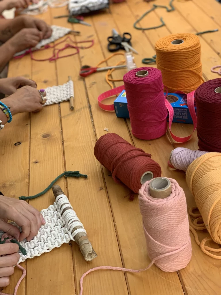 Bobines de cordes de coton pour macramé sur table avec participantes autour qui tissent leur tenture murale