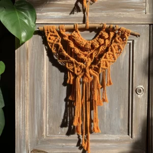 Macramé orange, accroché à un meuble cérusé