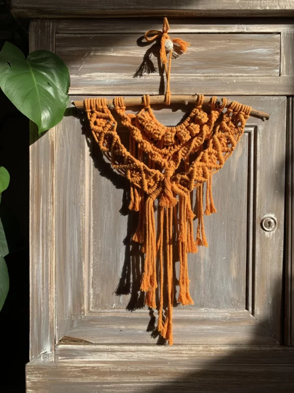 Macramé orange, accroché à un meuble cérusé