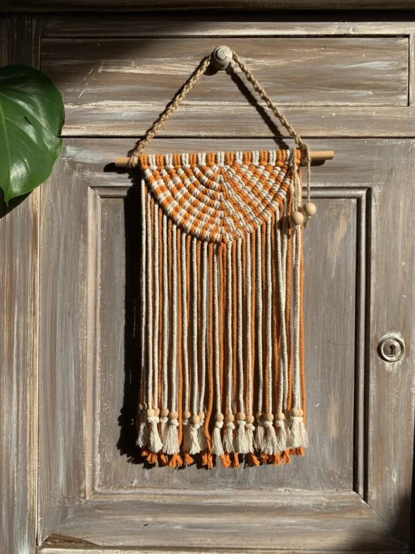 Macramé orange et blanc, demi cercle accroché à un meuble cérusé