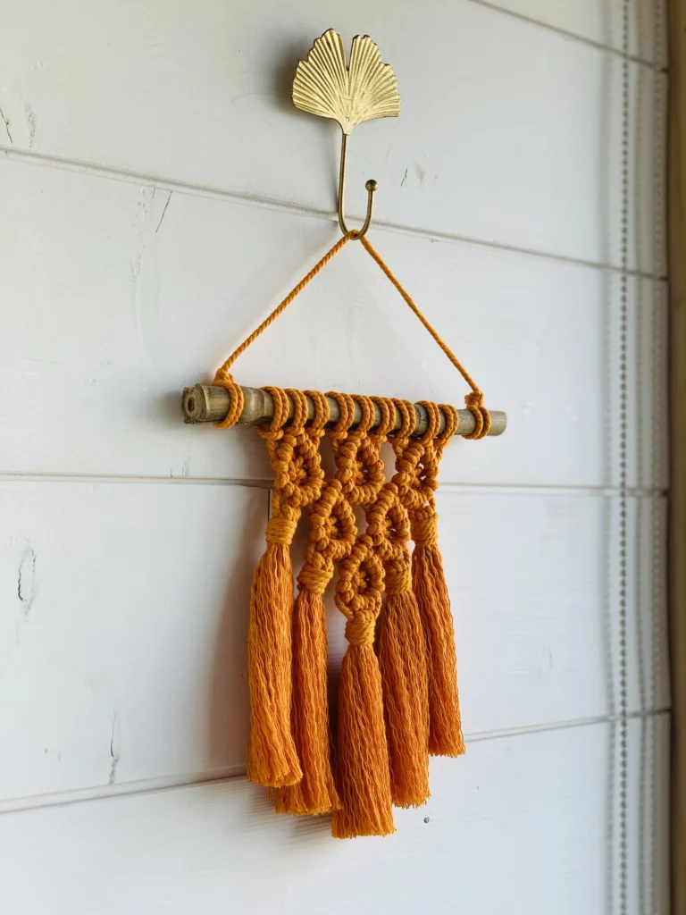 Macramé orange accroché à une patère gingko doré sur bardage bois blanc